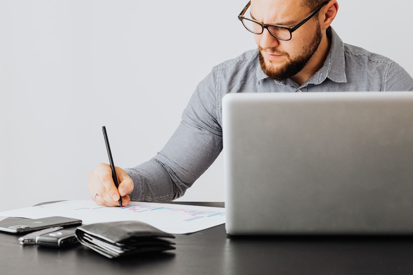 Homem fazendo anotações num papel ao lado do laptop