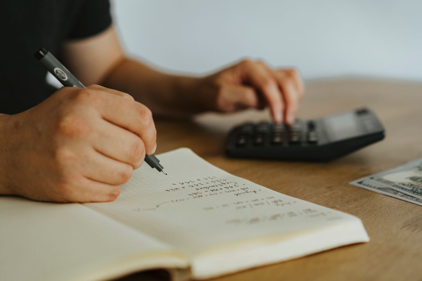 Pessoa anotando contas num caderno ao lado de uma calculadora